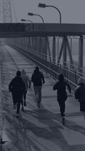 grupo de runners abrigados corriendo cruzando un puente